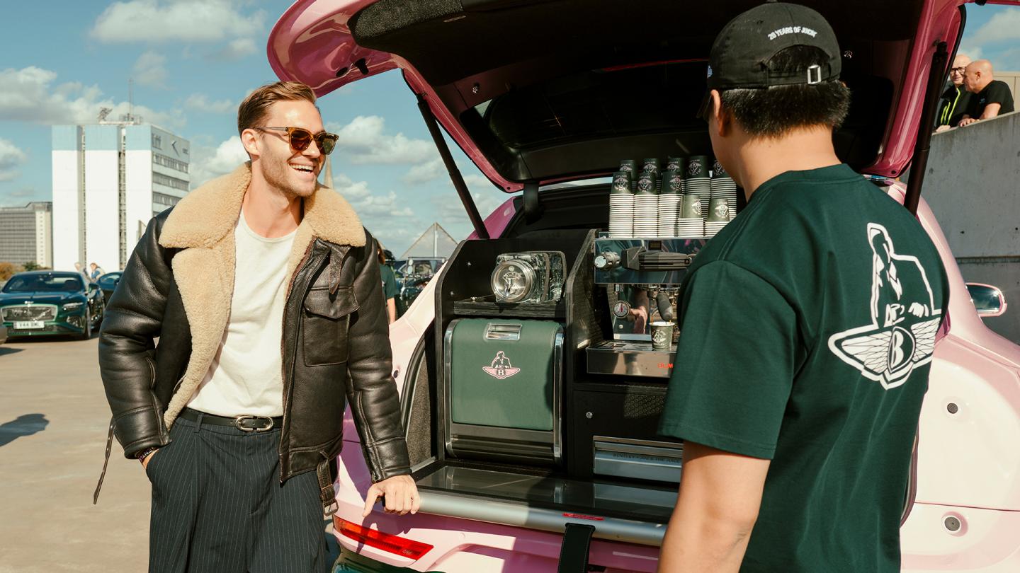 Two people looking at an espresso machine in the back of a Bentley Bentayga