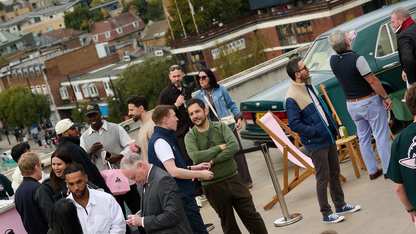 People mingling on rooftop with vintage cars in the background